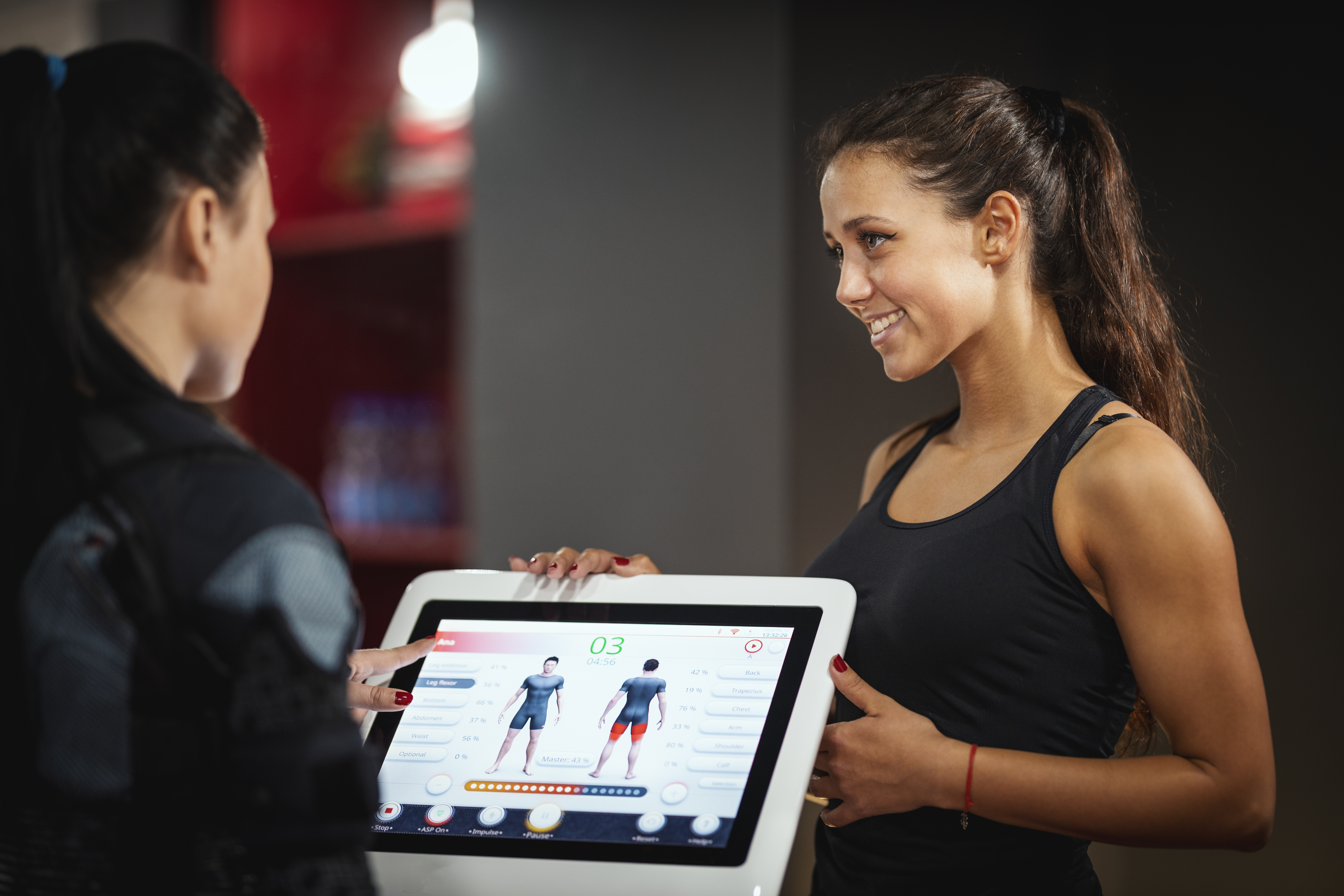 A athletic woman smiling as a personal trainer points to a fitness tracking display showing body composition data, highlighting how to lose body fat keep muscle.