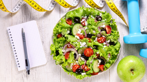 Lifestyle diets that work, featuring a healthy salad, fresh fruit, exercise equipment and a food journal for balanced weight management.
